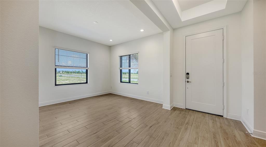 An empty room with light wood-look flooring, white walls, two windows, and a white door — 2234 LADY PALM LOOP, BRADENTON, FL