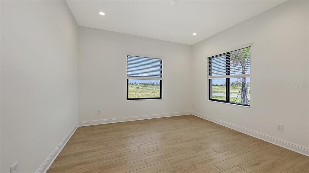 An empty room features light wood-look tile flooring, white walls, and two windows with blinds — 2234 LADY PALM LOOP, BRADENTON, FL
