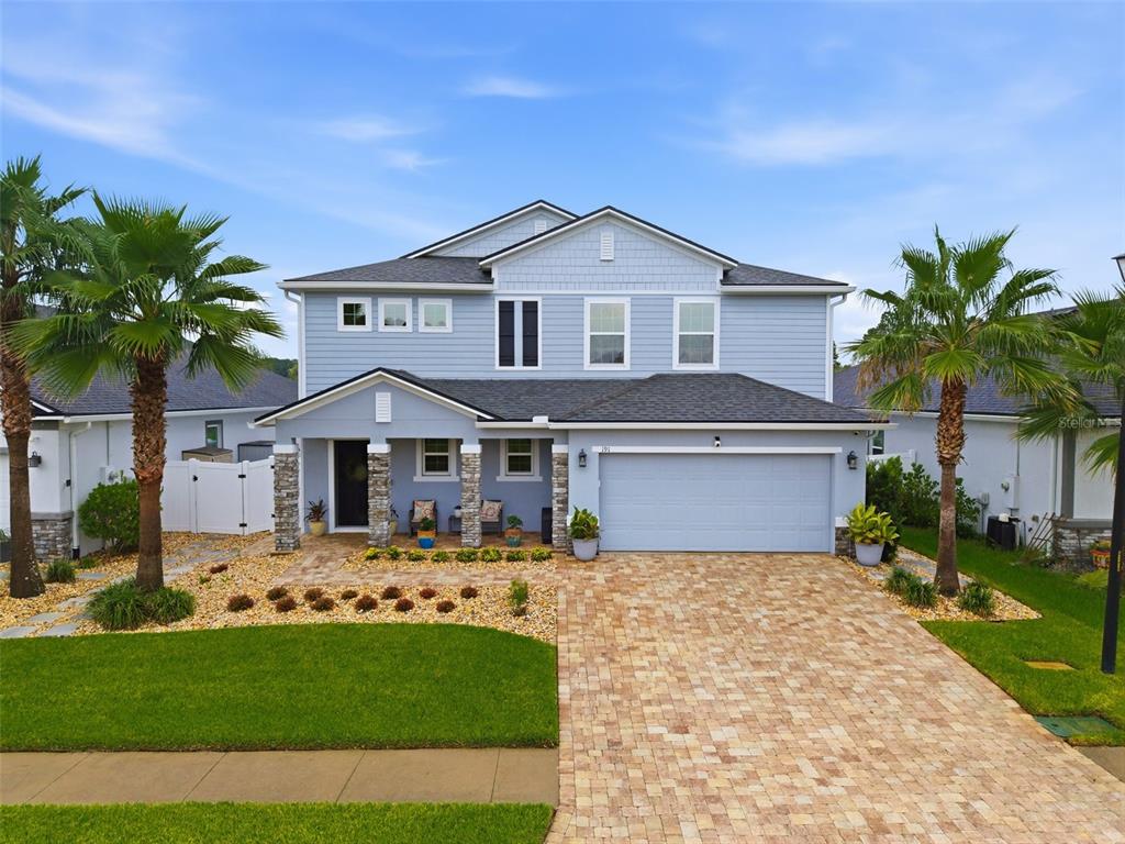 A two-story light blue house features a stone-accented porch, a paved driveway, and palm trees — 191 SANDSTONE DRIVE, ST AUGUSTINE, FL
