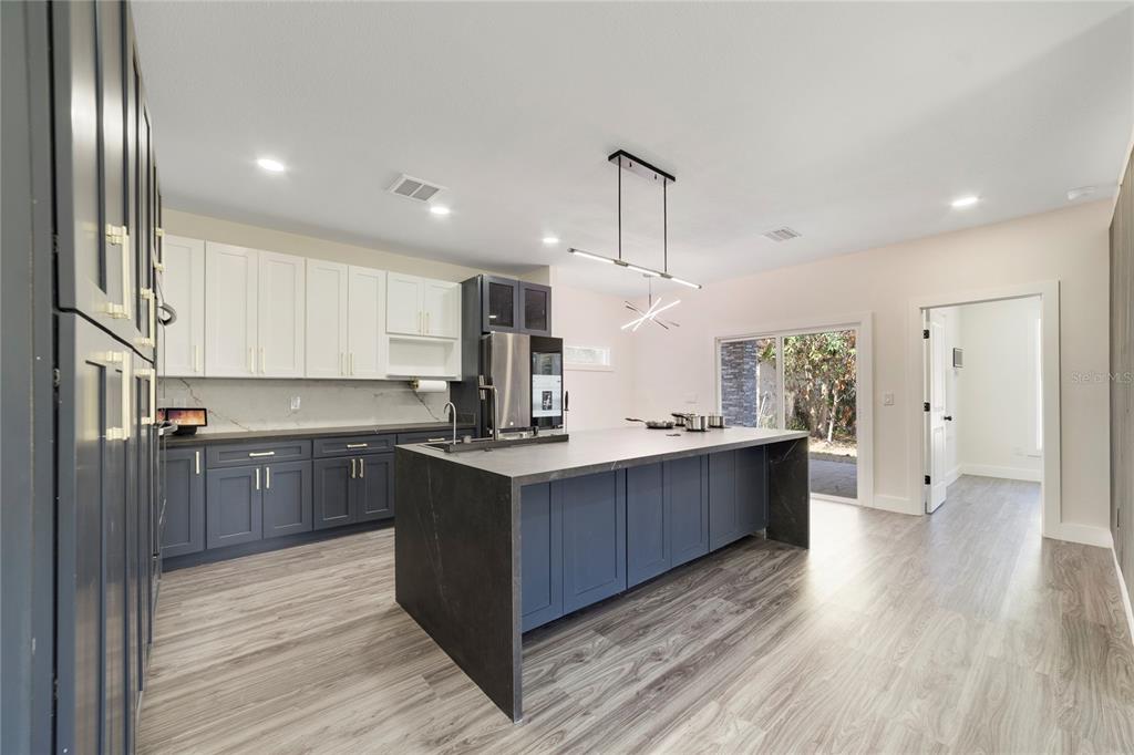 A modern kitchen features dark blue lower cabinets, white upper cabinets, and a large stone island — 1013 RANDALL STREET, ORLANDO, FL