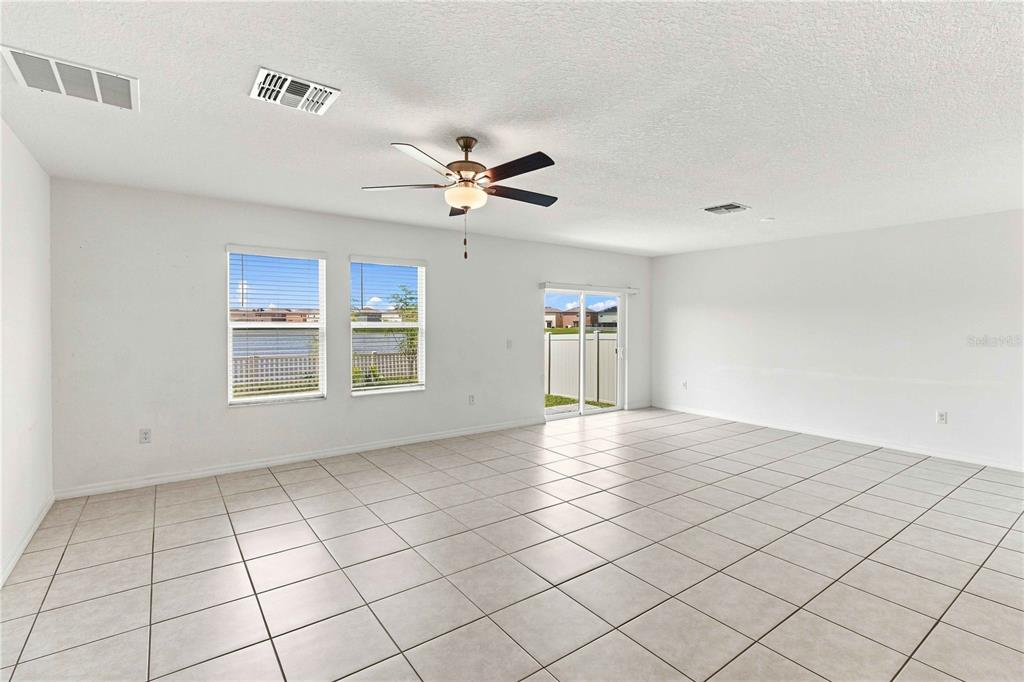 An empty living room features white walls, light tile flooring, a ceiling fan, and sliding doors — 5375 BLUE HORIZON WAY, WIMAUMA, FL