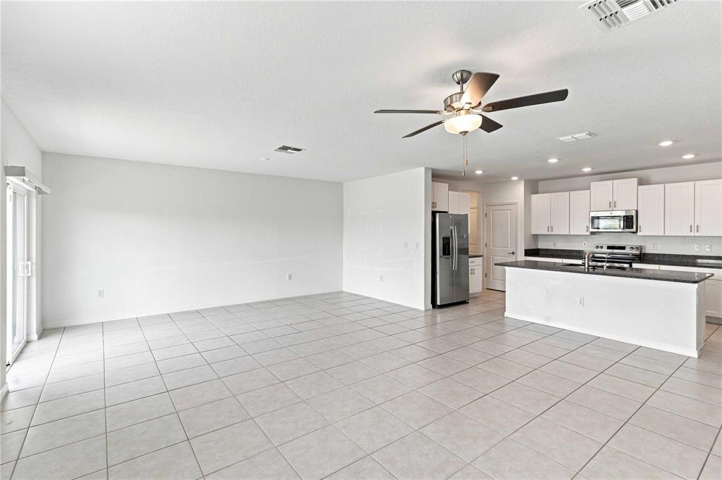 An open-concept living area features light-colored tile flooring, a ceiling fan, and a kitchen island — 5375 BLUE HORIZON WAY, WIMAUMA, FL