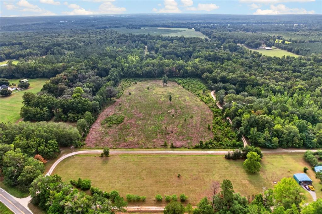 An aerial view shows a cleared lot bordered by trees and a dirt road — NW 239, ALACHUA, FL