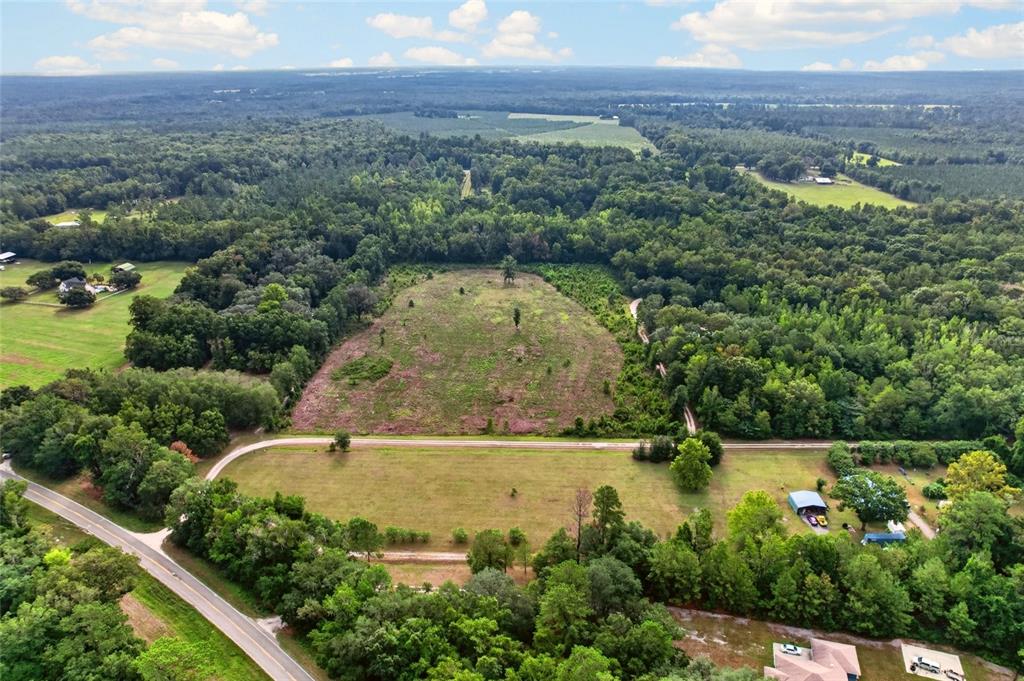 An aerial view shows a cleared lot bordered by trees, a road, and nearby houses — NW 239, ALACHUA, FL