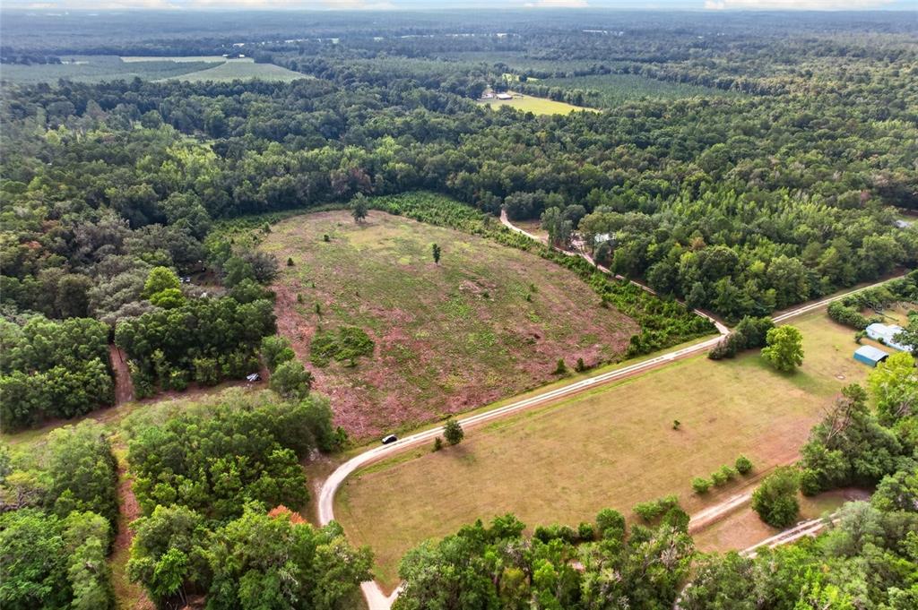 An aerial view shows a large, partially cleared field surrounded by dense forest and dirt roads — NW 239, ALACHUA, FL