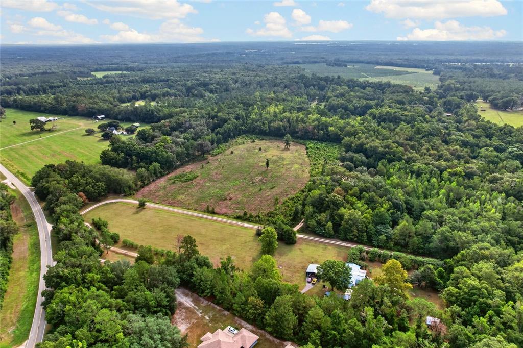 An aerial view shows a rural property with open fields, forested areas, and a house — NW 239, ALACHUA, FL