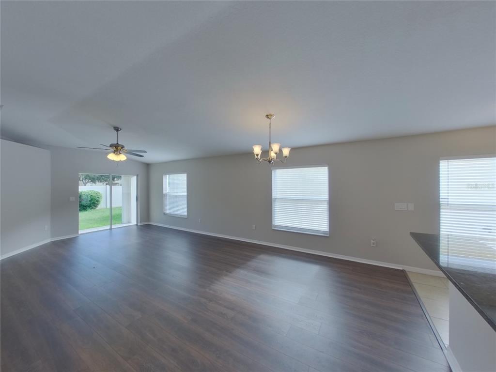 An empty living room features dark wood-look flooring, a ceiling fan, and a chandelier — 15512 TELFORD SPRING DRIVE, RUSKIN, FL