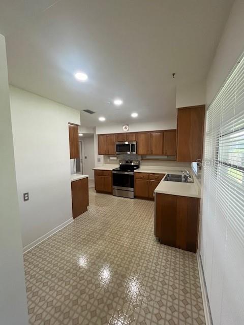 A kitchen features wood cabinets, stainless steel appliances, and a patterned vinyl floor — 1630 PICARDY CIRCLE, CLEARWATER, FL