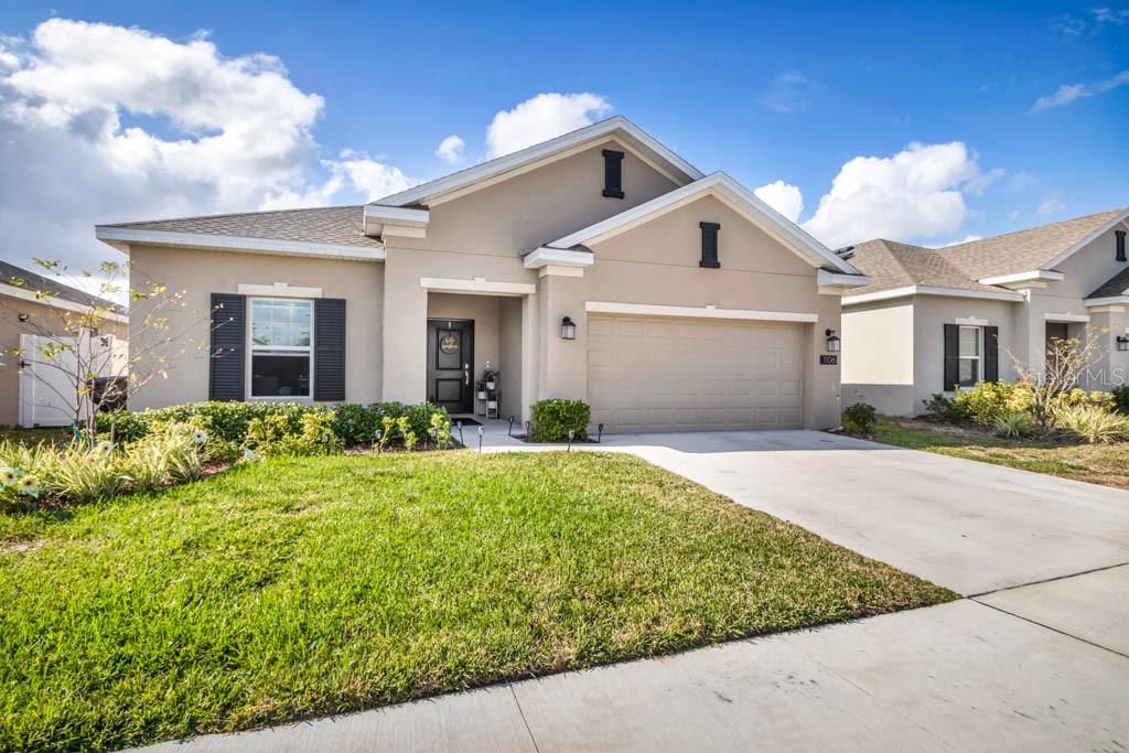 A single-story suburban house with a beige stucco exterior, a two-car garage, and a lawn — 1106 JAMES PAUL RD, DAVENPORT, FL
