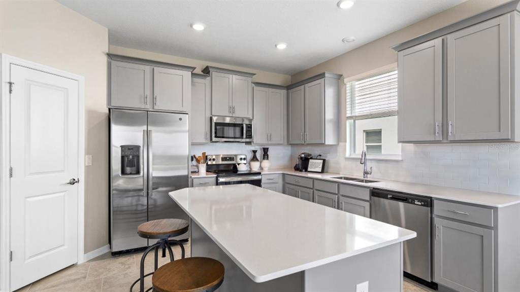A modern kitchen features gray cabinets, stainless steel appliances, and a white quartz island — 1106 JAMES PAUL RD, DAVENPORT, FL