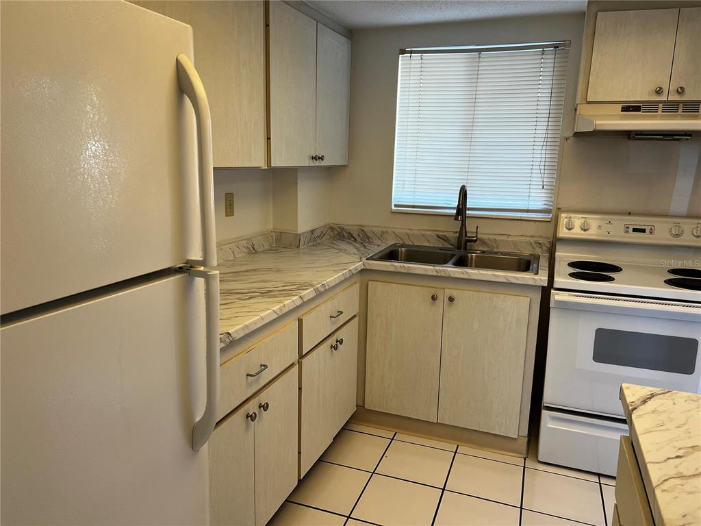 A kitchen features white appliances, light wood cabinets, and marble-patterned laminate countertops — 4112 HERON WAY UNIT B106, BRADENTON, FL