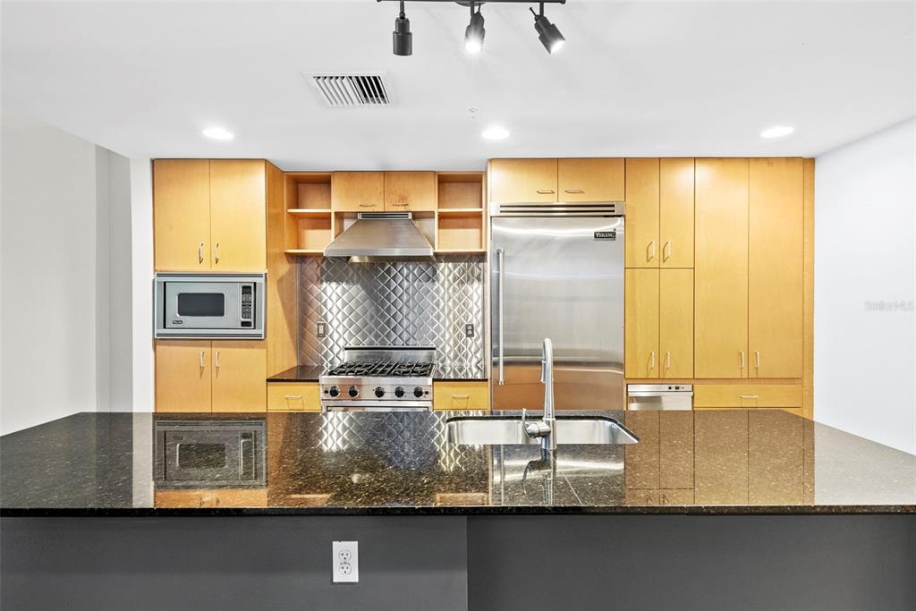 A modern kitchen features light wood cabinetry, stainless steel appliances, and a dark granite island — 1120 E KENNEDY BOULEVARD UNIT 618, TAMPA, FL