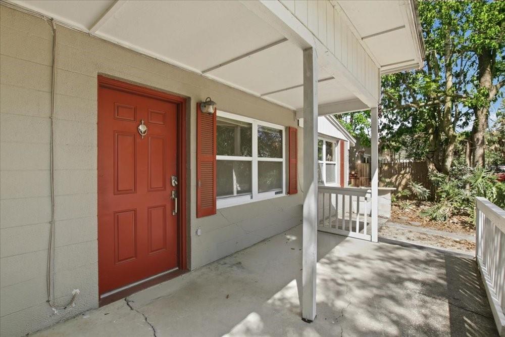 A covered concrete porch features a red front door and a window with red shutters — 1319 BESSMOR ROAD, WINTER PARK, FL