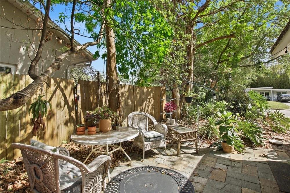 A stone patio features wicker chairs, a round table, and potted plants near a wooden fence — 1319 BESSMOR ROAD, WINTER PARK, FL