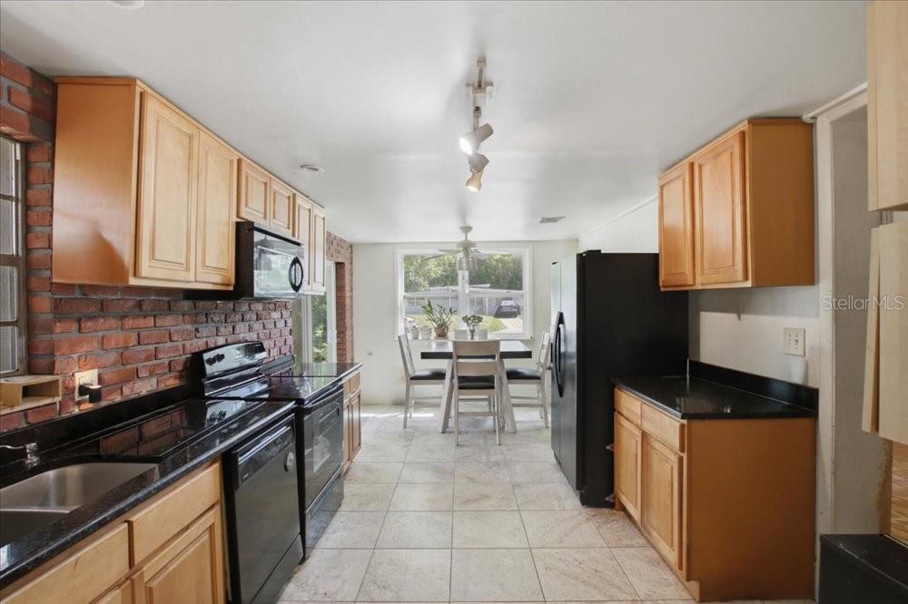 A kitchen features light wood cabinets, black countertops, a brick wall, and a dining area — 1319 BESSMOR ROAD, WINTER PARK, FL