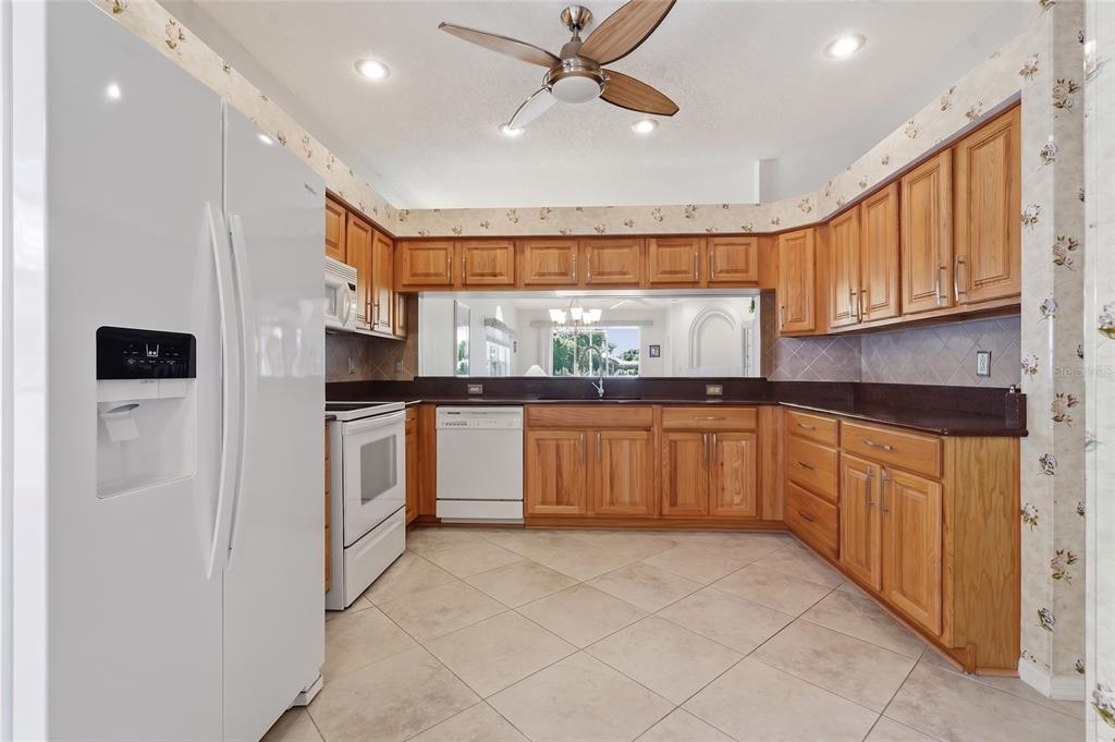 A kitchen with oak cabinets, dark countertops, white appliances, and floral wallpaper above the cabinets — 1063 DARTFORD DRIVE, TARPON SPRINGS, FL