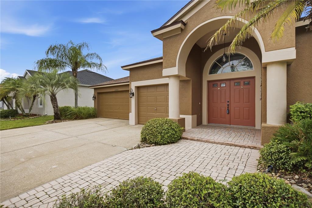 A tan house with a brick paver walkway, double front doors, and a three-car garage — 25843 RISEN STAR DRIVE, WESLEY CHAPEL, FL