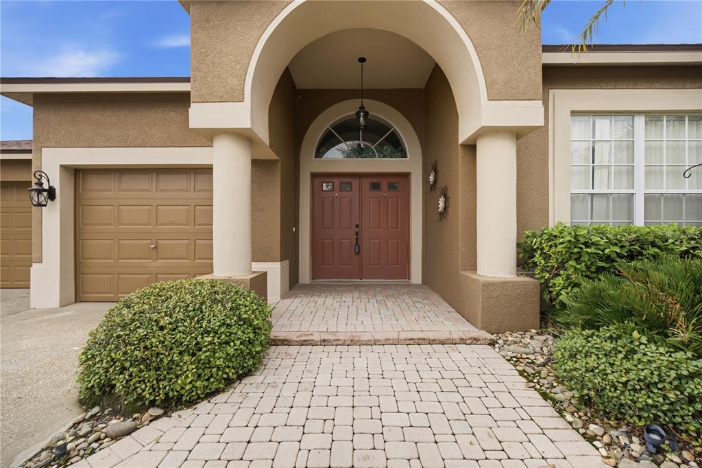 The exterior of a house features a tan stucco facade, a brick walkway, and double doors — 25843 RISEN STAR DRIVE, WESLEY CHAPEL, FL