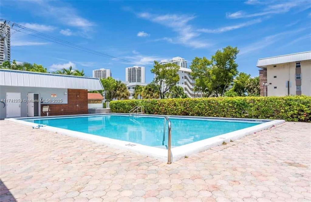 A rectangular outdoor swimming pool is surrounded by a paved patio and a green hedge — 3750 NE 170TH STREET UNIT 311, NORTH MIAMI BEACH, FL
