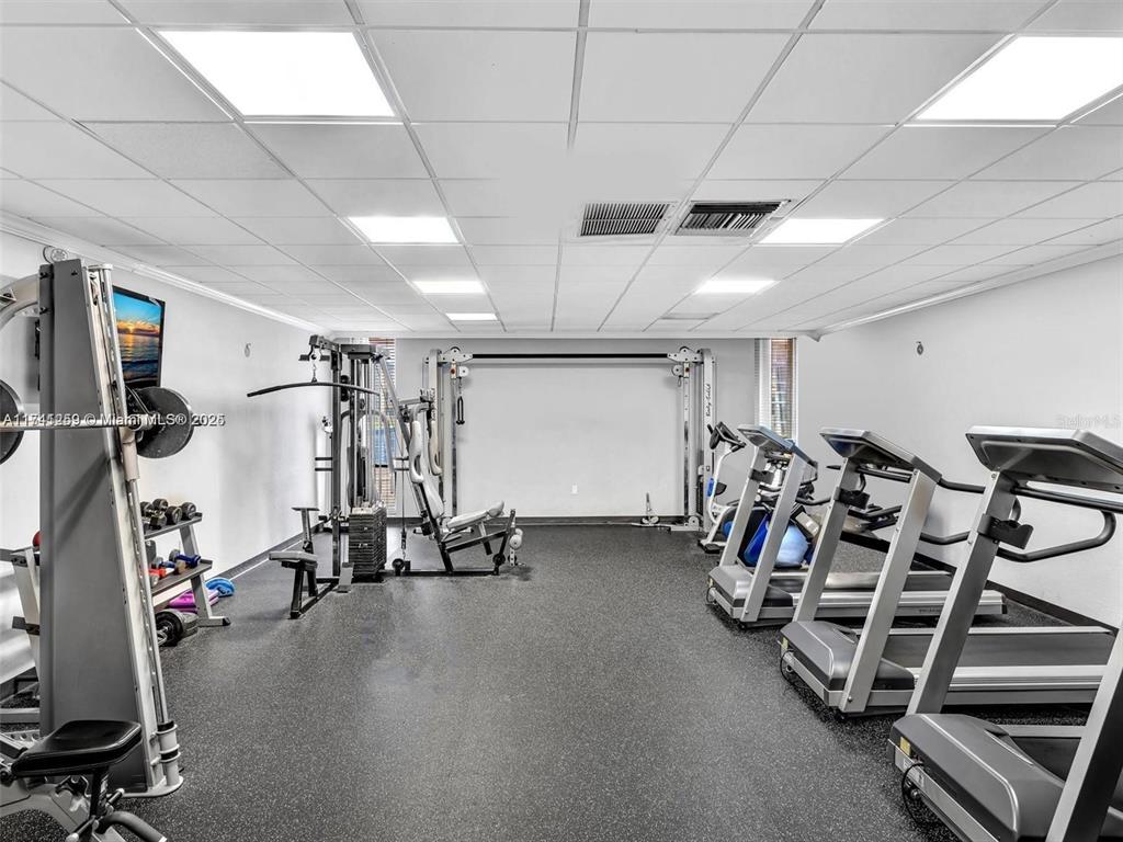 This gym features various exercise machines, rubber flooring, and a drop ceiling with recessed lighting — 3750 NE 170TH STREET UNIT 311, NORTH MIAMI BEACH, FL