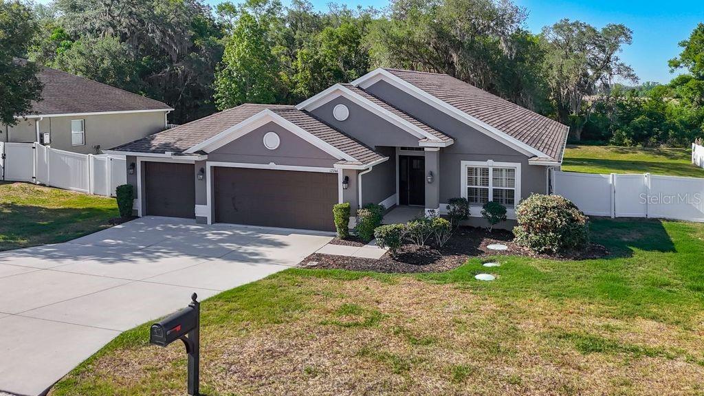 A gray single-story house with a two-car garage and a white vinyl fence — 12244 LOOPBACK DRIVE, SAN ANTONIO, FL