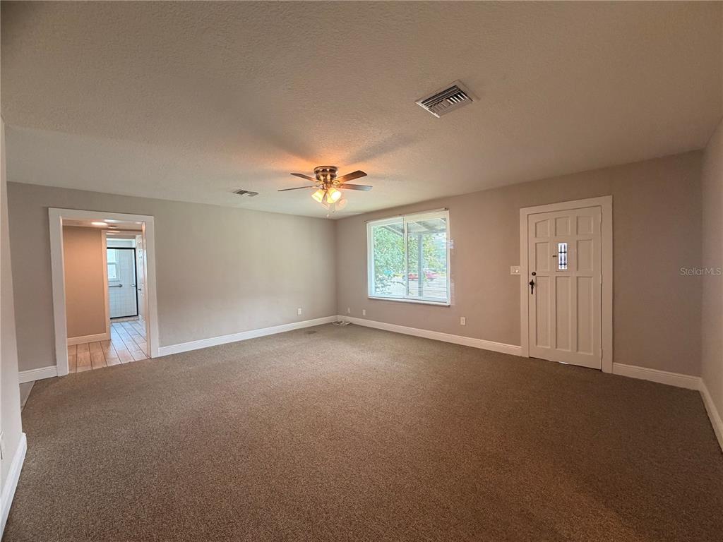 A carpeted living room features a ceiling fan, a window, and a white entry door — 144 N PARK AVENUE, APOPKA, FL