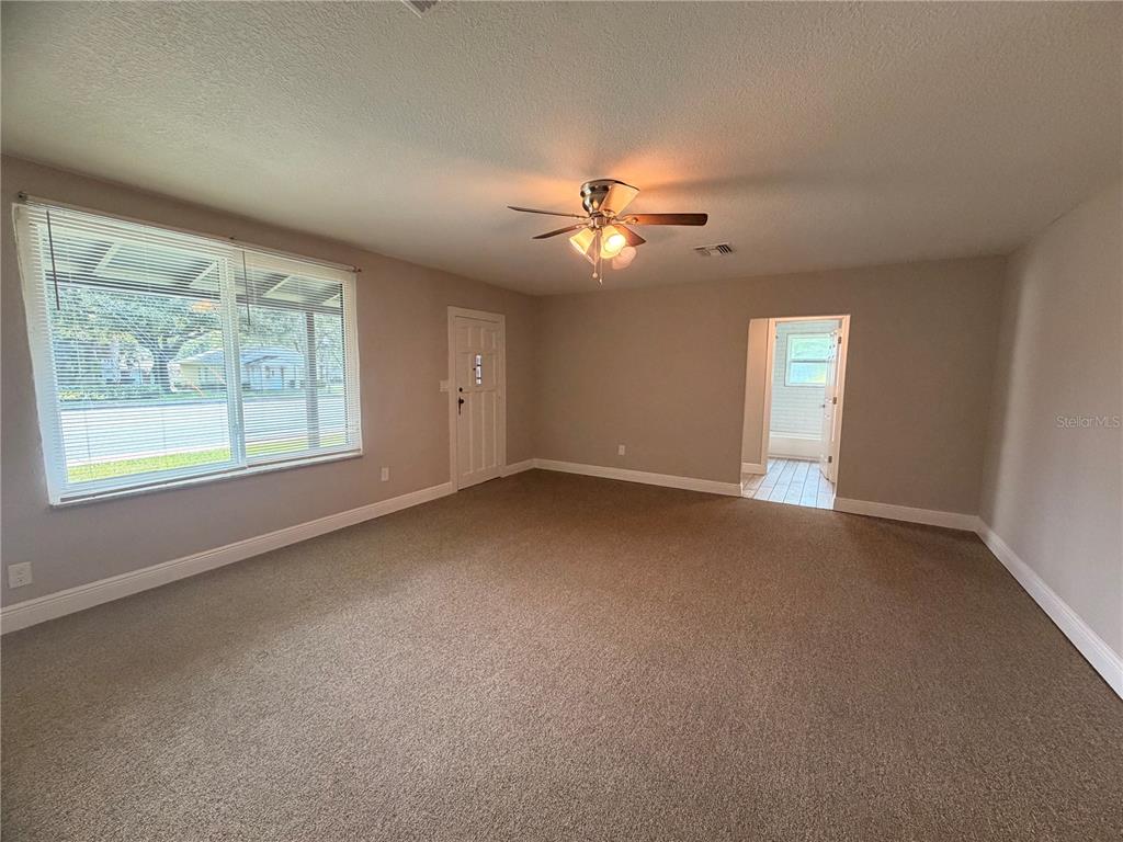 An empty living room features beige carpeting, a ceiling fan, and a large window — 144 N PARK AVENUE, APOPKA, FL