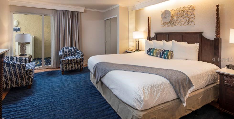 A hotel bedroom features a king bed, two patterned armchairs, and a sliding glass door — 5500 GULF BOULEVARD UNIT 2249, ST PETE BEACH, FL
