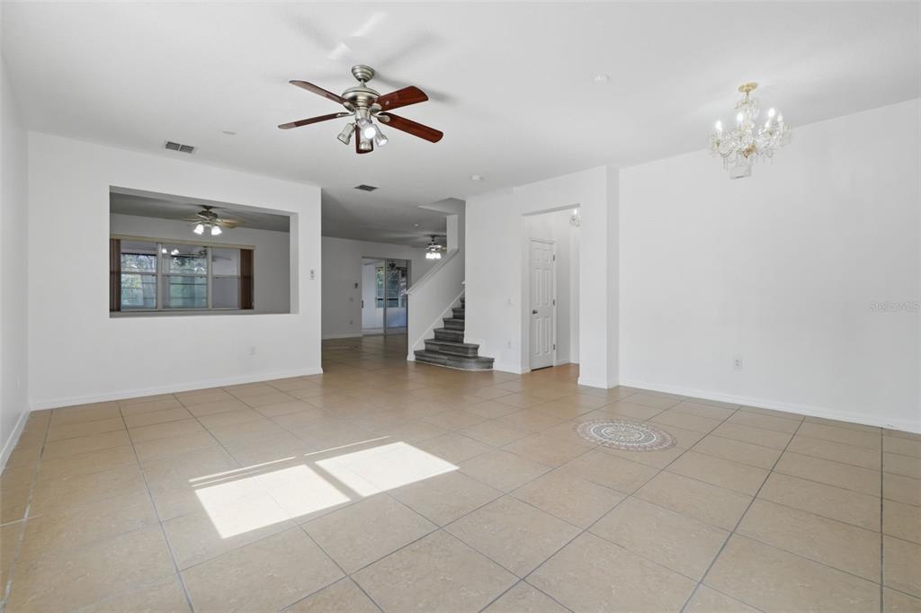 An open-concept living area features light-colored tile flooring, a ceiling fan, and a staircase — 2830 PAYNES PRAIRIE CIRCLE, KISSIMMEE, FL