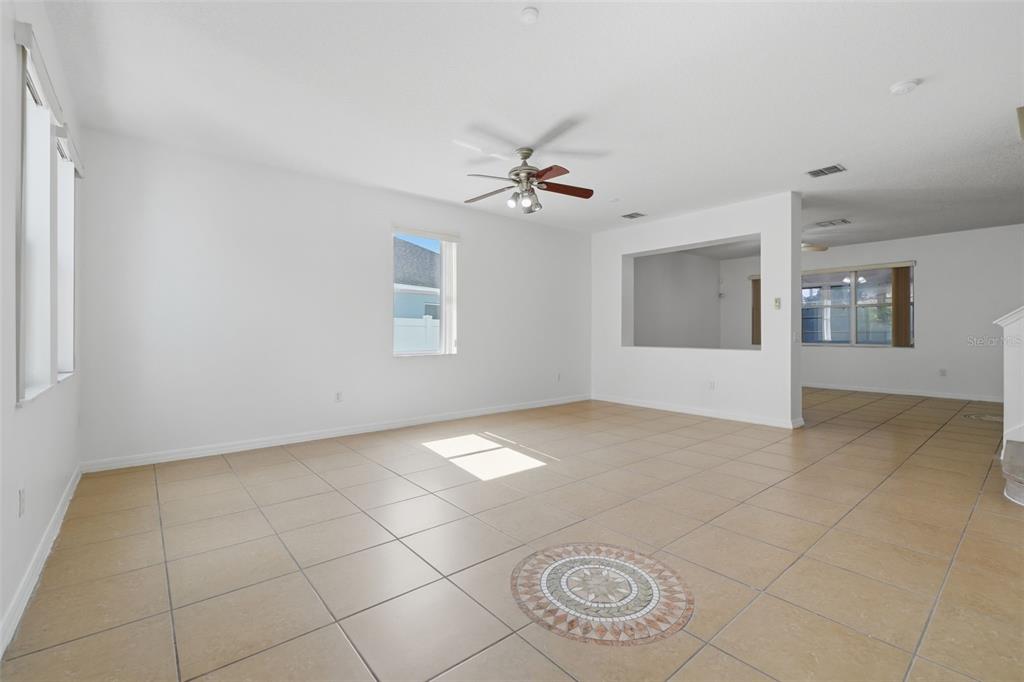 A spacious living room features white walls, tan tile flooring, and a ceiling fan — 2830 PAYNES PRAIRIE CIRCLE, KISSIMMEE, FL