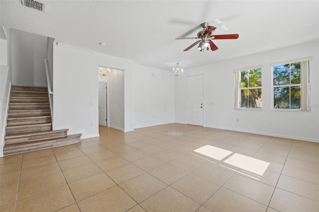 An open living area features tan tile flooring, a wooden staircase, and a ceiling fan — 2830 PAYNES PRAIRIE CIRCLE, KISSIMMEE, FL