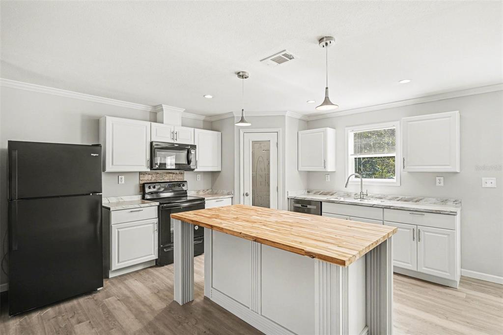 A kitchen features white cabinets, a butcher block island, black appliances, and light wood flooring — 23950 BASS ROAD, ASTOR, FL
