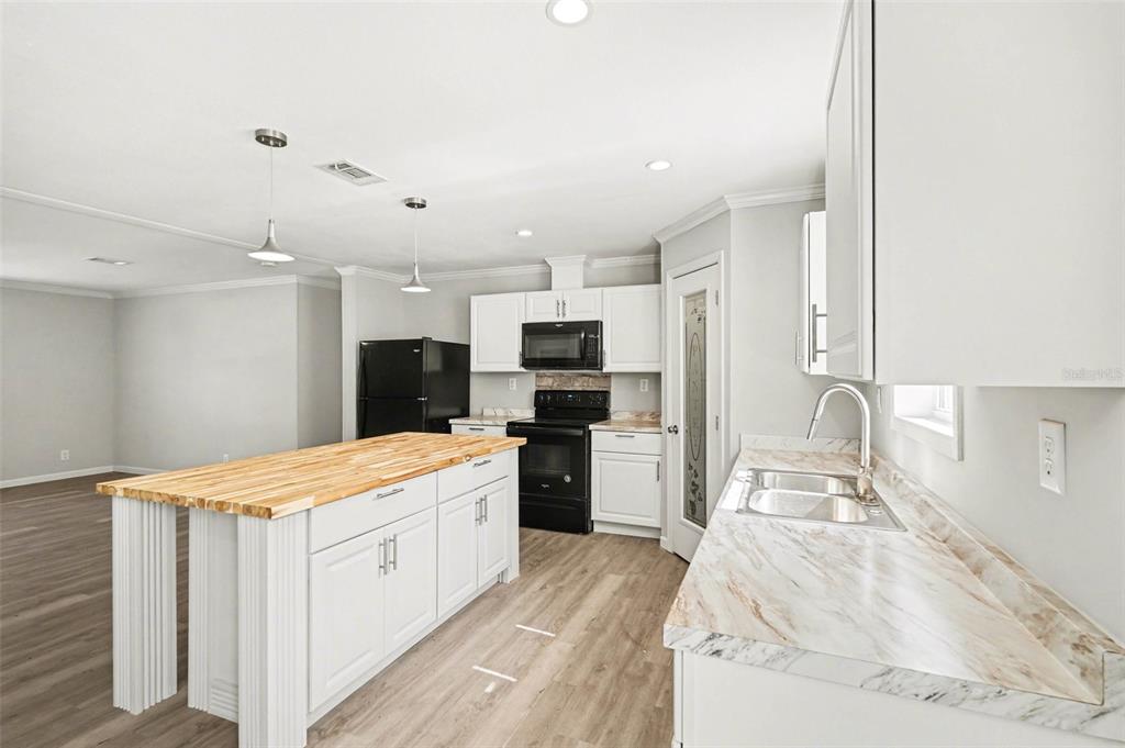 A kitchen with white cabinets, a wood-topped island, black appliances, and marble-patterned countertops — 23950 BASS ROAD, ASTOR, FL