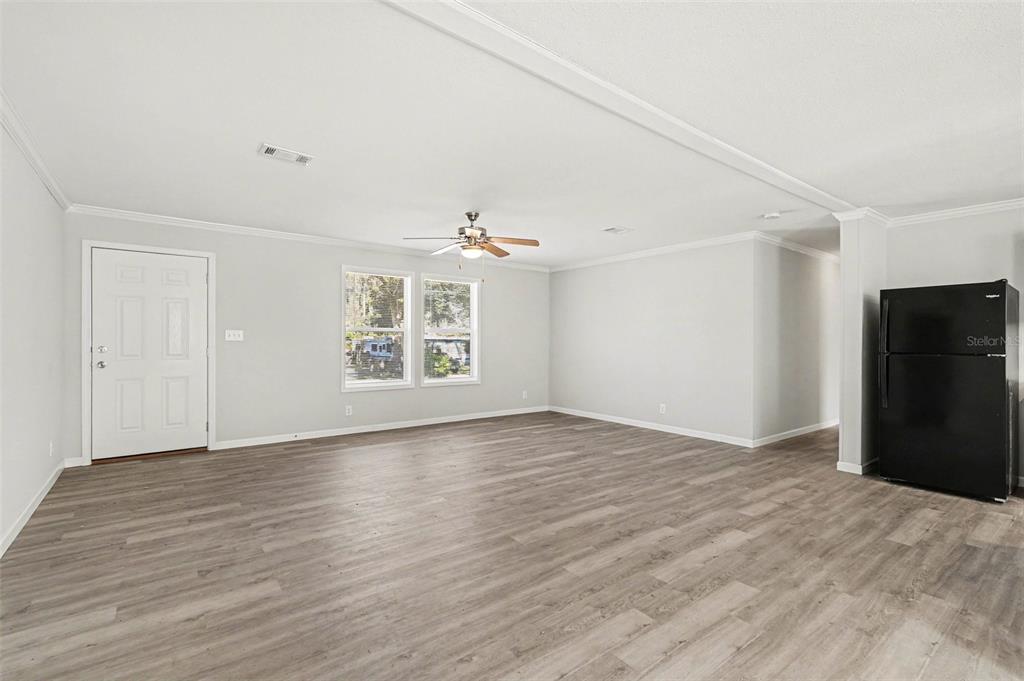 An open living area features light gray walls, wood-look flooring, a ceiling fan, and a refrigerator — 23950 BASS ROAD, ASTOR, FL