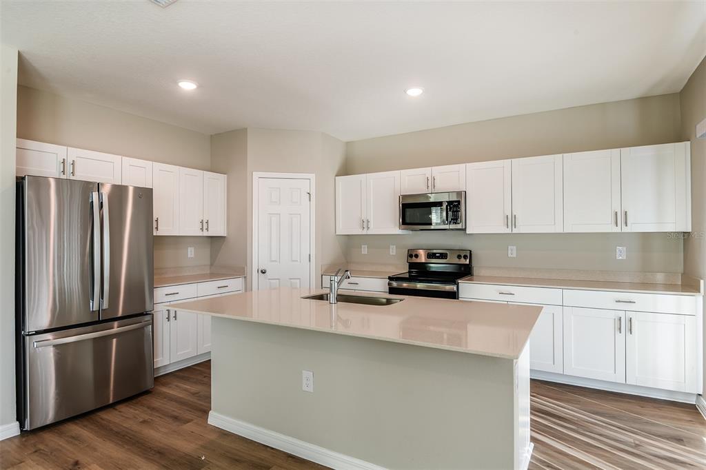 A kitchen with white cabinets, stainless steel appliances, a center island, and wood-look flooring — 1589 SAGE AVENUE, HAINES CITY, FL