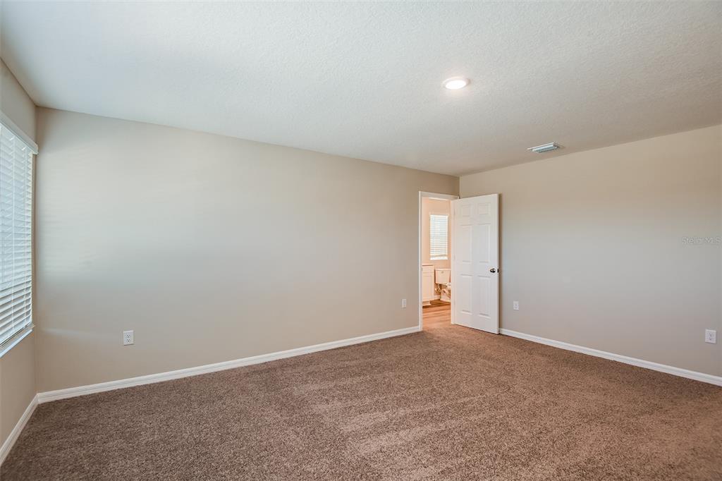 A bedroom with beige walls, brown carpet, and an open door leading to a bathroom — 1589 SAGE AVENUE, HAINES CITY, FL