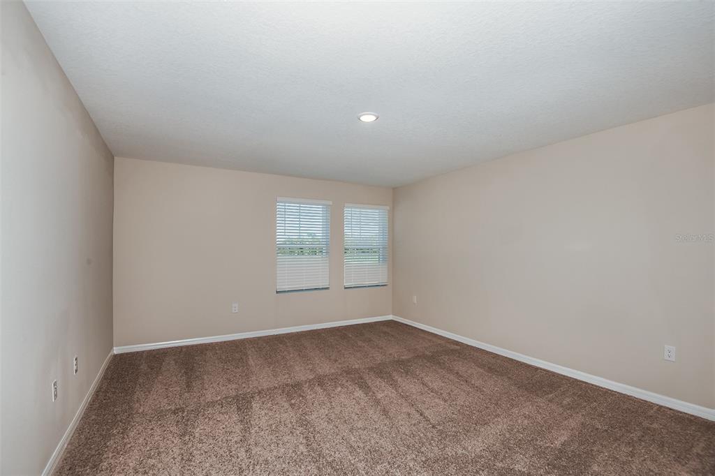An empty bedroom with beige walls, brown carpeting, and two windows with white blinds — 1589 SAGE AVENUE, HAINES CITY, FL