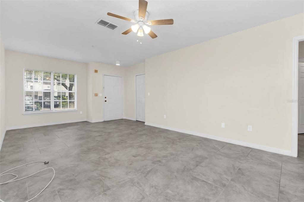 An empty living room features gray tile flooring, beige walls, and a ceiling fan — 4328 S KIRKMAN ROAD UNIT 1311, ORLANDO, FL