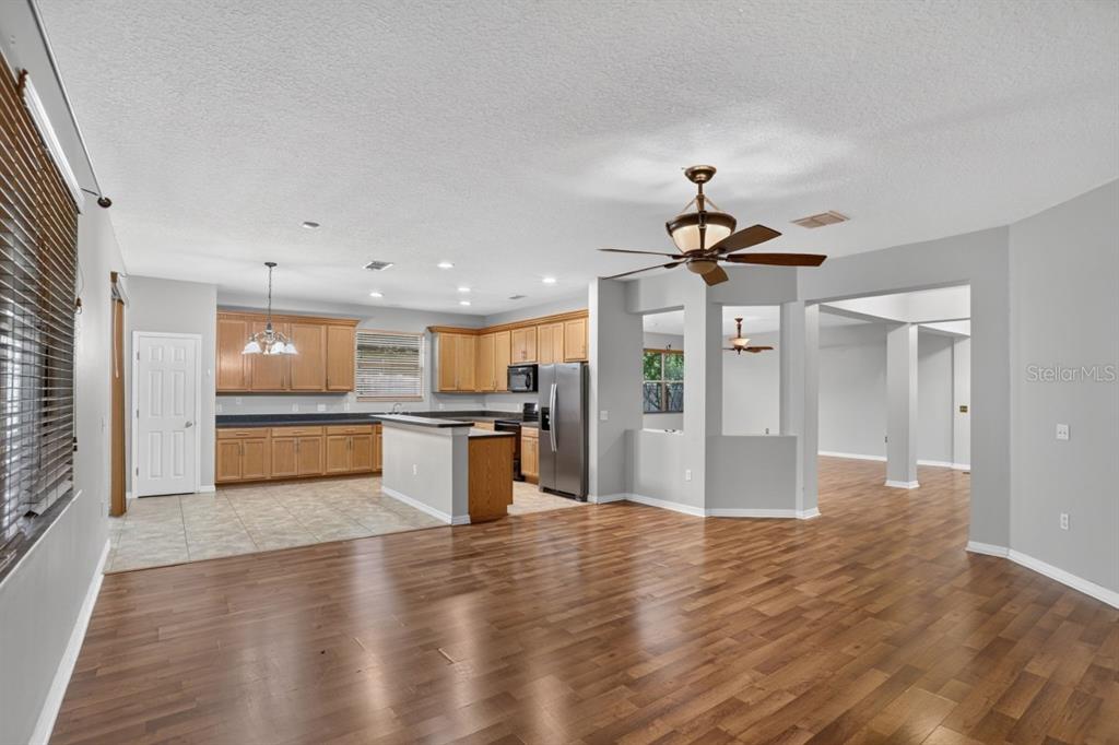An open-concept kitchen with wood cabinets and a breakfast bar overlooks a wood-floored living area — 3730 CEDAR HAMMOCK TRAIL, ST CLOUD, FL
