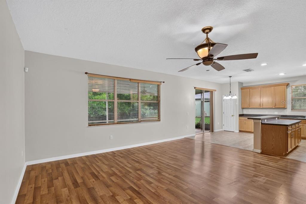 A living room with wood-look flooring, a ceiling fan, and an adjacent open-concept kitchen — 3730 CEDAR HAMMOCK TRAIL, ST CLOUD, FL