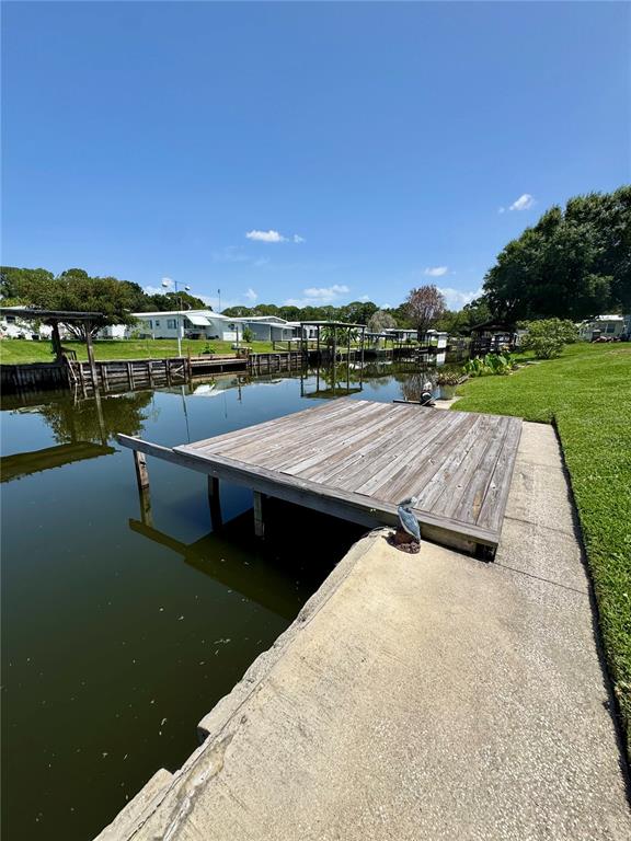 A wooden dock extends over a canal next to a concrete walkway and grassy lawn — 119 JANA CIRCLE, AUBURNDALE, FL