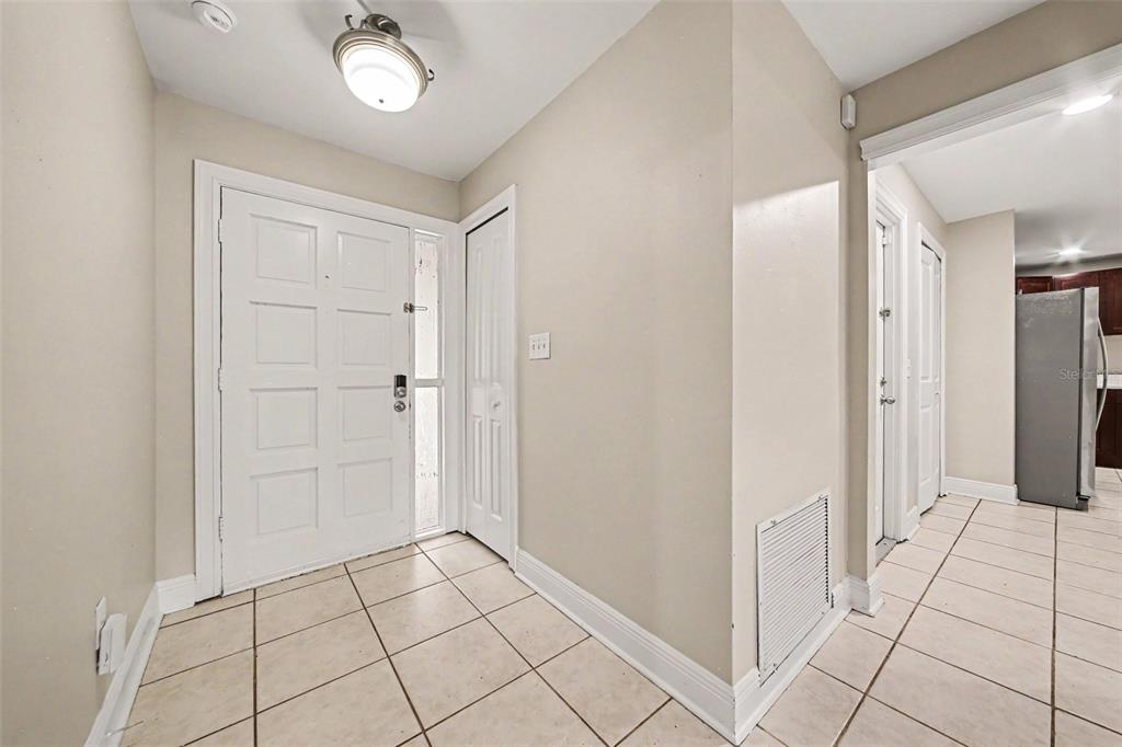 An entryway with a white front door, tiled floor, and a view into the kitchen — 612 HEATHER BRITE CIRCLE, APOPKA, FL