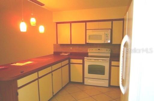 A kitchen features light-colored cabinets, a white stove, a microwave, and a wooden breakfast bar — 4033 ANNA DRIVE, APOPKA, FL