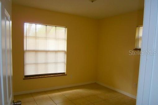 An empty room with yellow walls, tiled floors, and two windows with closed blinds — 4033 ANNA DRIVE, APOPKA, FL