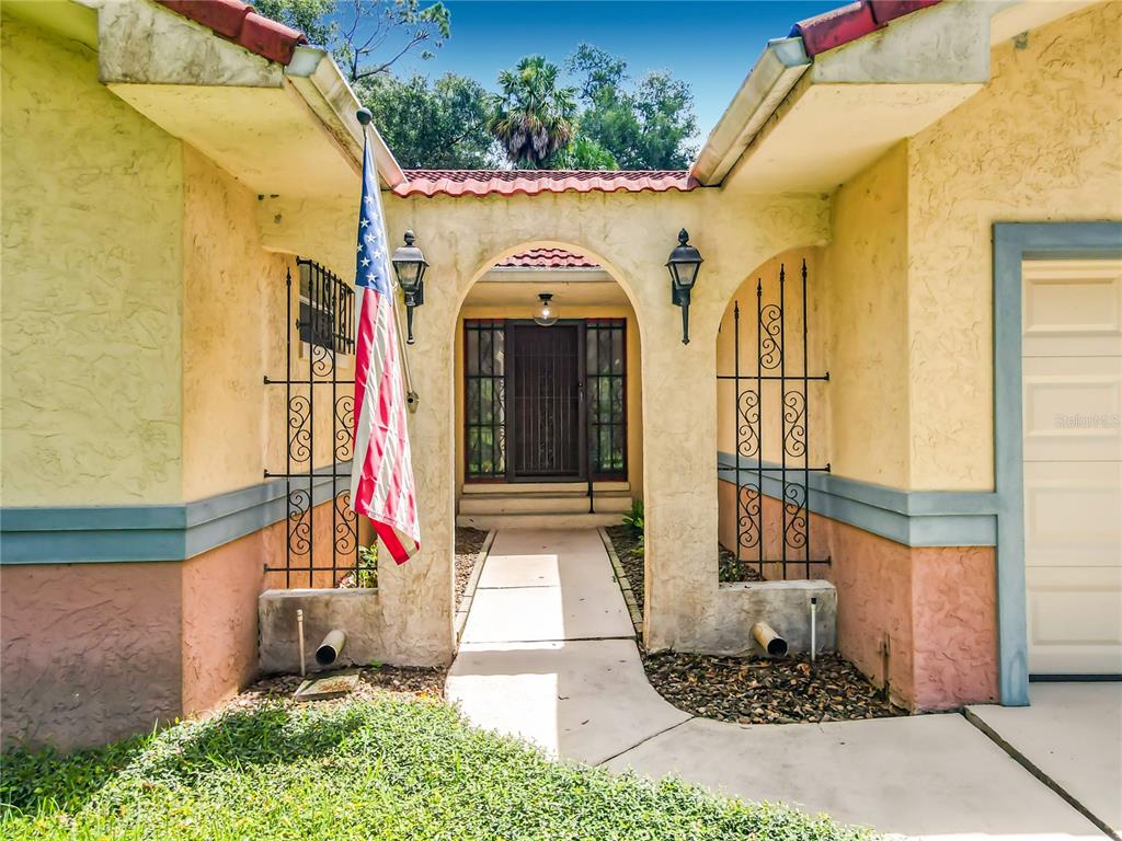 The exterior of a house features a stucco facade, an arched entryway, and an American flag — 2269 COUNTRY CLUB DRIVE, DELAND, FL