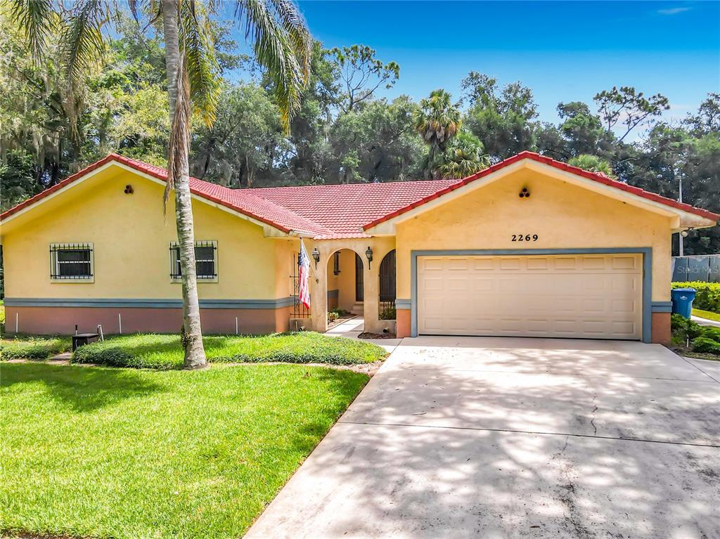 A single-story house with a red tile roof, yellow stucco walls, and a two-car garage — 2269 COUNTRY CLUB DRIVE, DELAND, FL