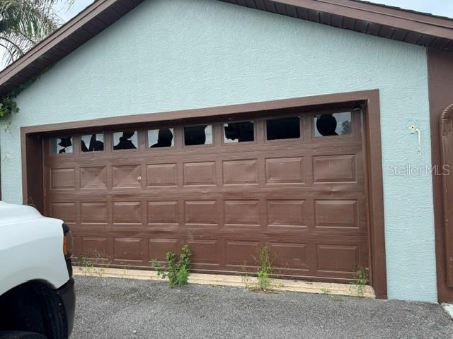 A brown garage door with broken windows is attached to a light blue stucco house — 2231 CR 543, SUMTERVILLE, FL