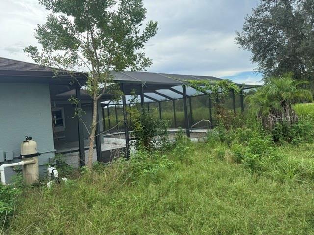 A view of a house exterior featuring a screened-in pool enclosure and overgrown yard — 2231 CR 543, SUMTERVILLE, FL