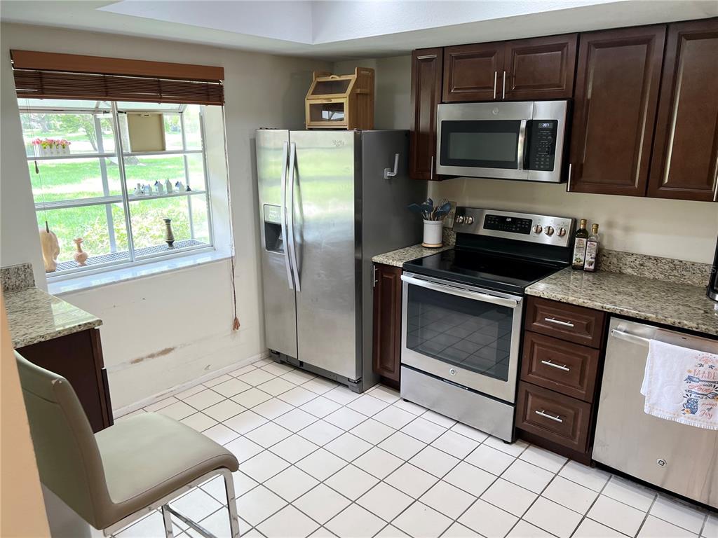 A kitchen features dark wood cabinets, stainless steel appliances, granite countertops, and a tile floor — 2297 LARK CIRCLE E UNIT C, PALM HARBOR, FL