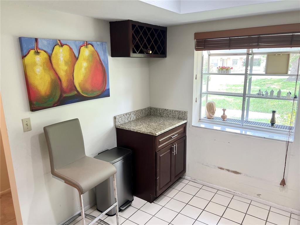A kitchen corner features a granite countertop, dark wood cabinets, a wine rack, and tile flooring — 2297 LARK CIRCLE E UNIT C, PALM HARBOR, FL